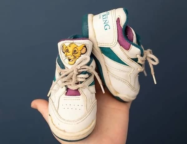 Small white Lion King Simba high top sneakers held in hand.