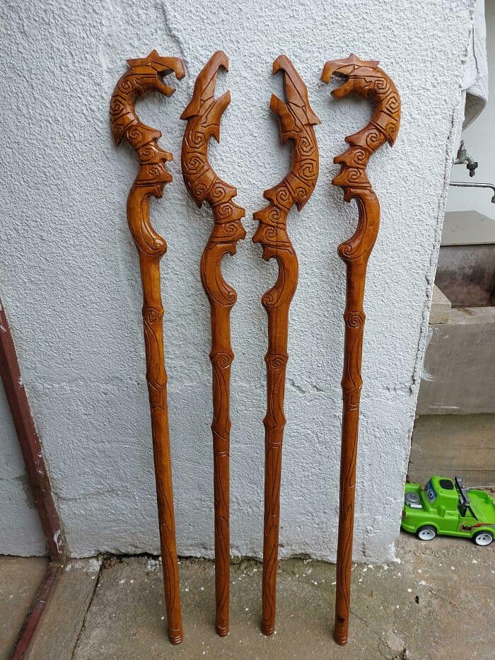 Four hand-carved wooden wizard staffs topped with intricate dragon heads. Detailed fantasy cosplay props.