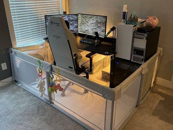 Computer desk and gaming chair surrounded by baby safety gate playpen fence.