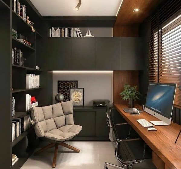Modern dark themed office with built-in shelving and comfortable beige reading chair.