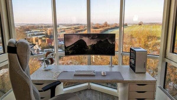Minimalist desk setup facing panoramic curved windows with expansive countryside view.