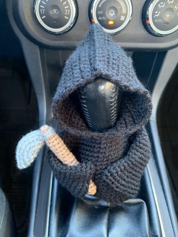 A creative knitting project featuring a crocheted Grim Reaper gear shift cover holding a scythe.