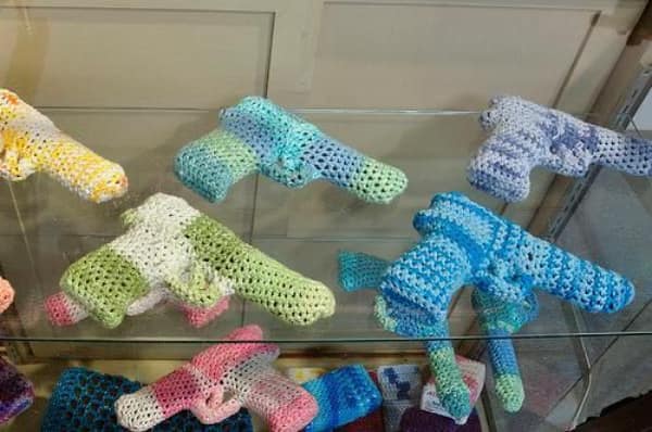 A display case filled with pastel and camouflage colored handguns made from yarn, a unique creative knitting project.