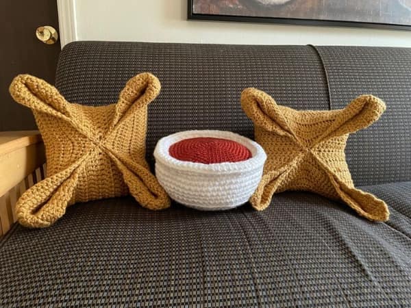 A set of creative knitting project pillows shaped like tortellini pasta and a bowl of tomato sauce.
