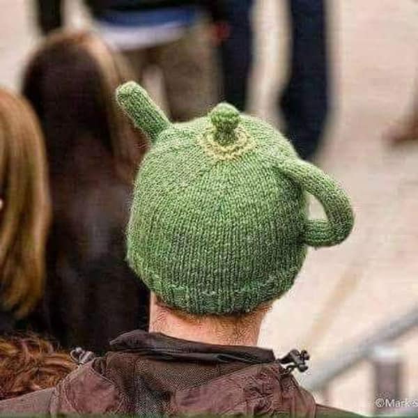 A man wearing a green creative knitting project hat shaped exactly like a teapot with a spout and handle.