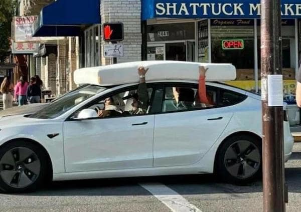 A driving fail showing passengers holding a mattress onto the roof of a Tesla with their bare hands.