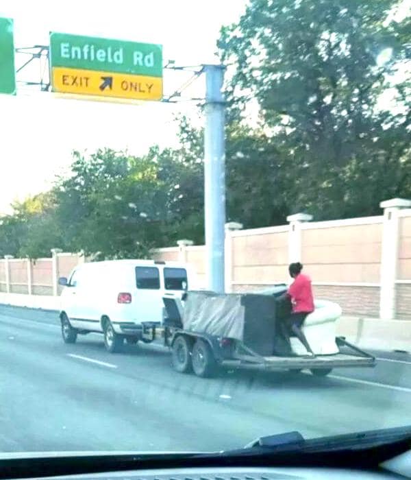 A bad driver photo of a person sitting on a couch on an open trailer while driving on a highway.