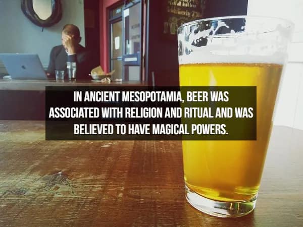 close-up of a bubbling lager sits in the foreground while a blurred figure works on a laptop behind it. The caption discusses the mystical side of facts about beer: "In ancient Mesopotamia, beer was... believed to have magical powers."