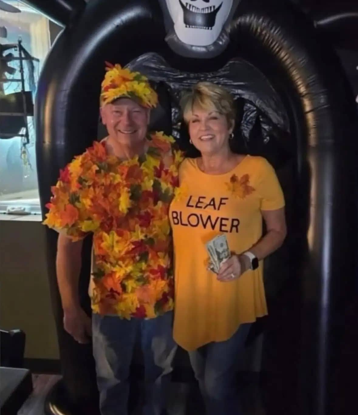 Middle-aged couple in a punny Halloween costume where one is a leaf and the other is a leaf blower.