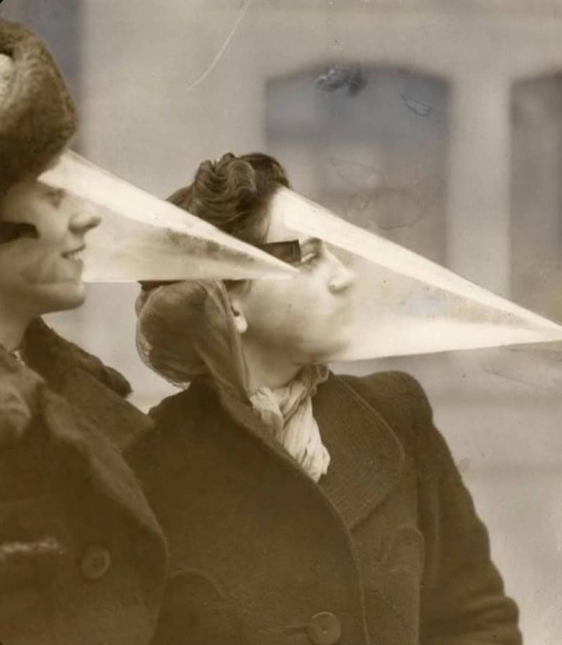 Two women wearing plastic cone-shaped face shields to protect them from the elements, a strange historical photo with no context