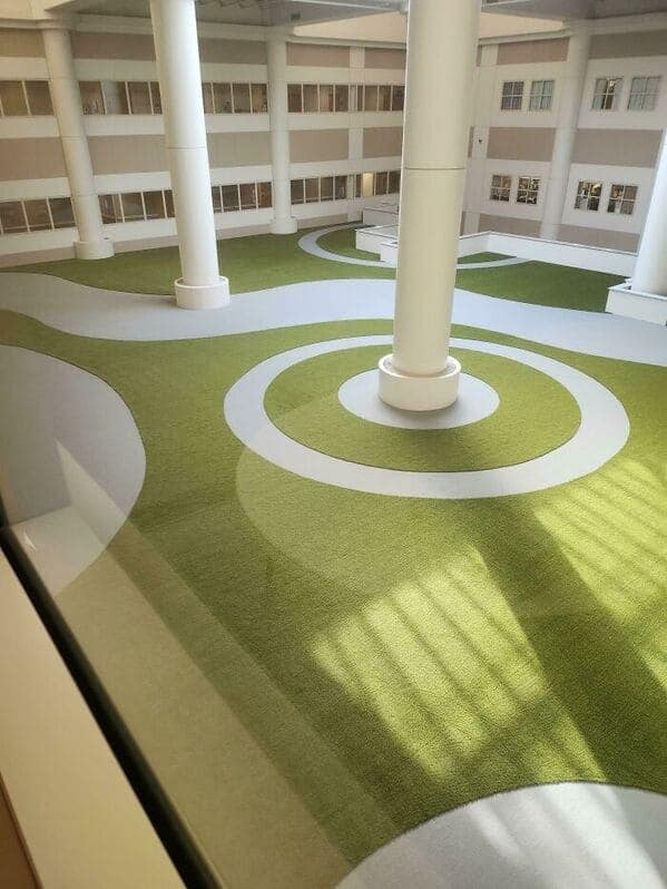 A liminal space creepy indoor courtyard with artificial green turf and large white pillars.