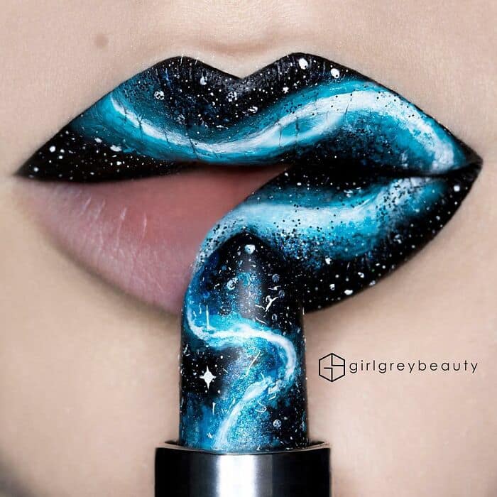 Cosmic and amazing lip art transforming the mouth into a glowing blue and black galaxy filled with bright stars, perfectly paired with a matching painted lipstick bullet in true, seamless Andrea Reed lip art fashion.