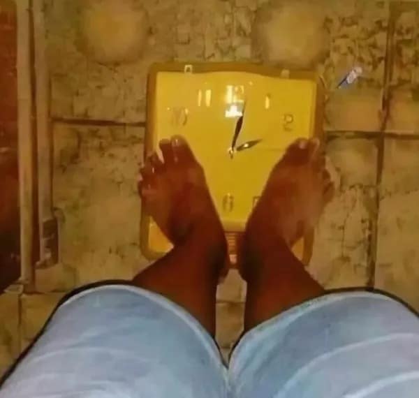 confusing and funny meme showing a first-person perspective of a person's bare feet standing on a yellow analog wall clock that has been placed on the floor to mimic a weight scale.