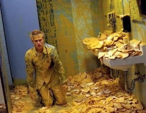 surreal and hilarious meme showing a man kneeling in a public bathroom that is completely buried in thousands of slices of bread and covered in a thick yellow substance, creating a scene of absolute, unexplained chaos.