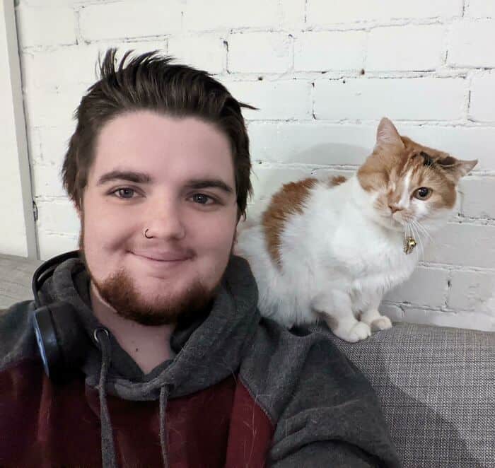 A man with brown hair and a beard sitting next to a white and ginger cat.