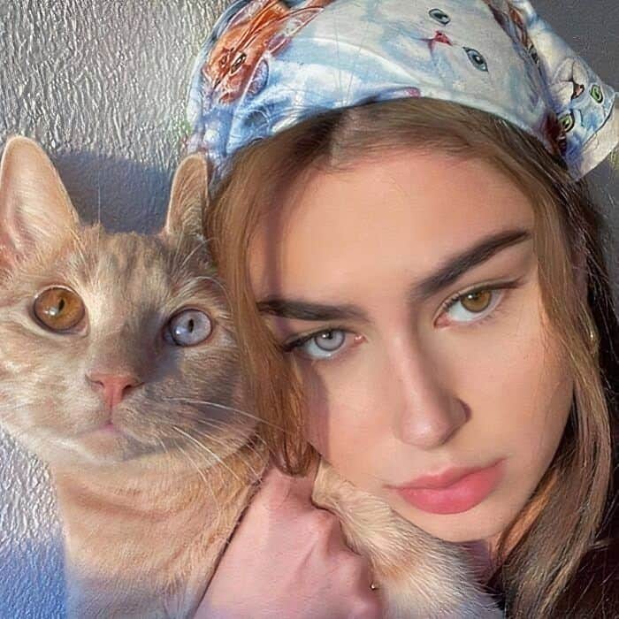 Young woman with heterochromia posing with a cat that has the same mismatched eye colors.