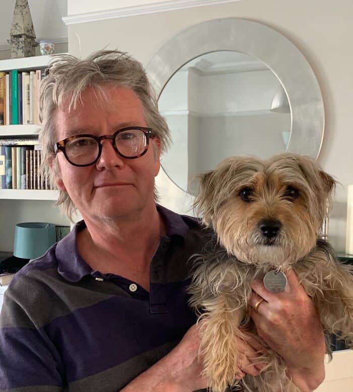 Man with messy grey hair and glasses holding a small scruffy terrier with similar features.