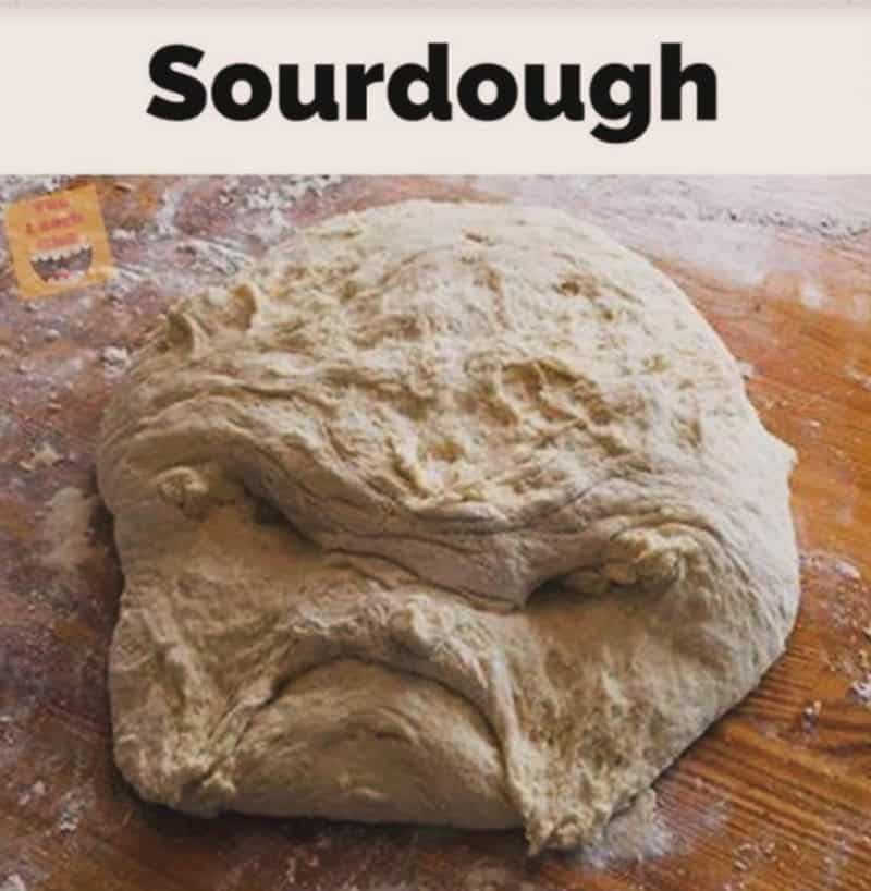 Grumpy looking raw sourdough dough on floured wooden surface labeled simply sourdough