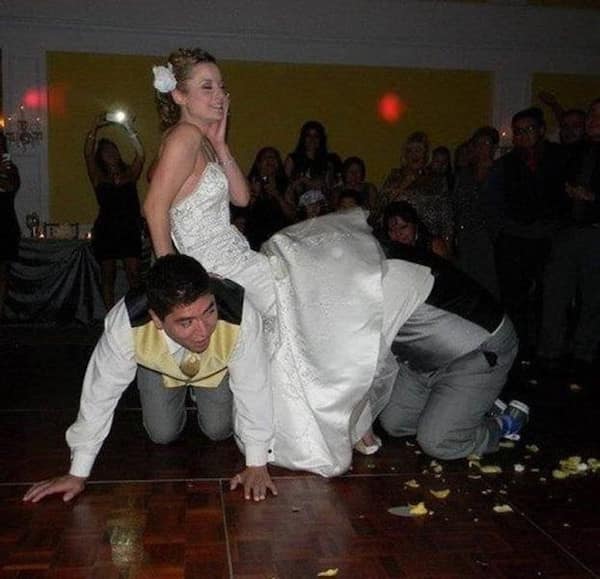 Bride sitting on backs of two groomsmen acting as a human chair.