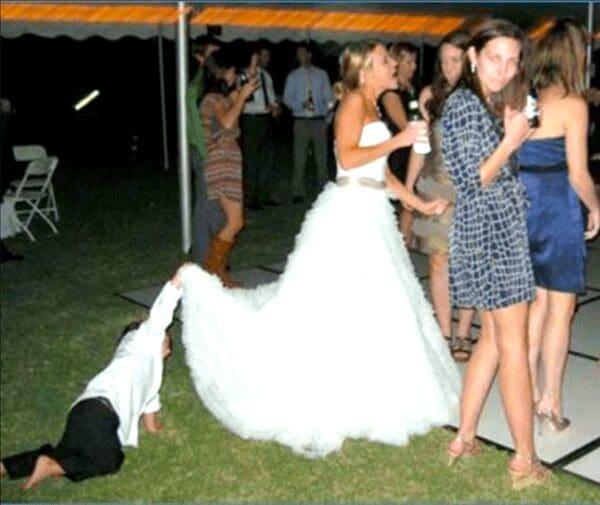 Child lying on grass pulling back on bride's dress train while being dragged.