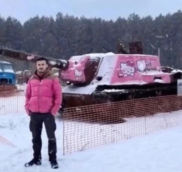 A hilarious subversion of expectations in this wholesome image where a man poses in the snow next to a massive military tank that has been painted bright pink and covered in Hello Kitty decals.
