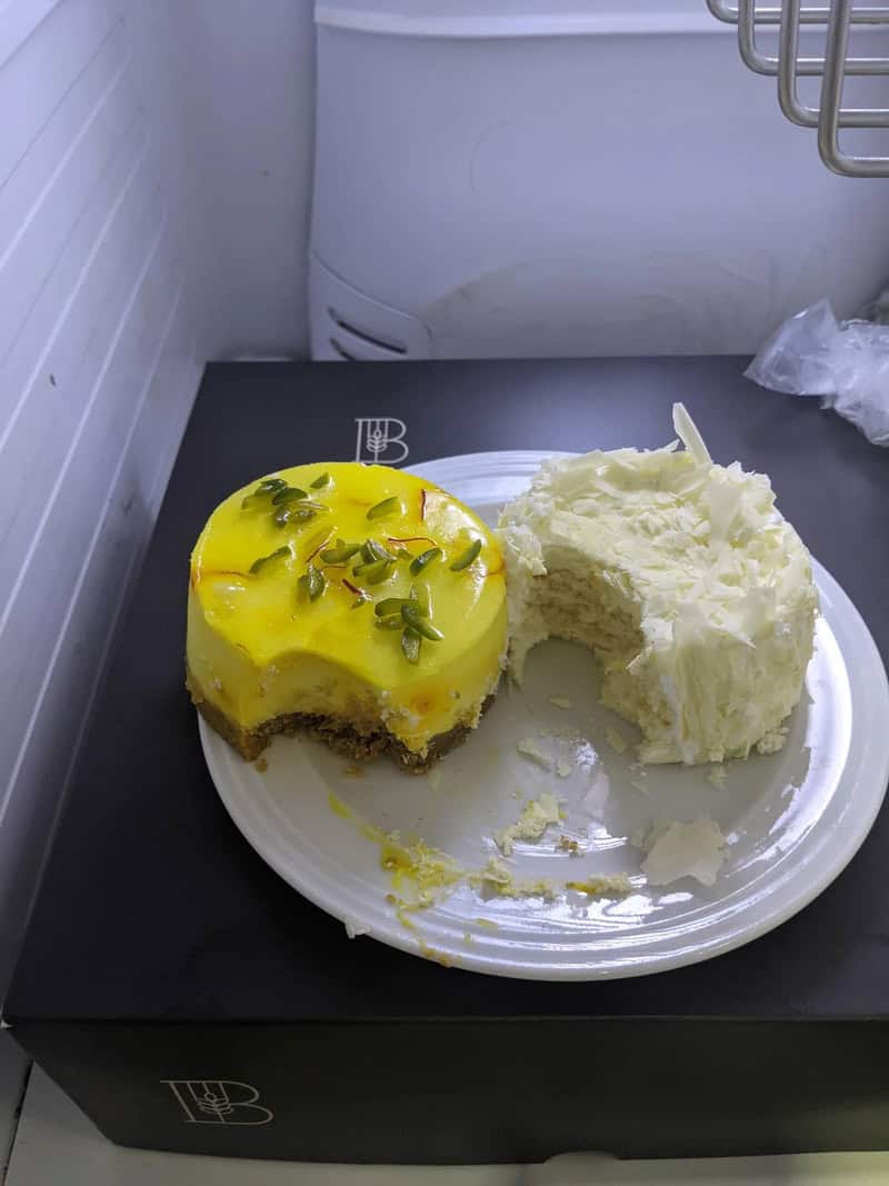 Two half-eaten fancy cakes stored uncovered on single plate inside office fridge