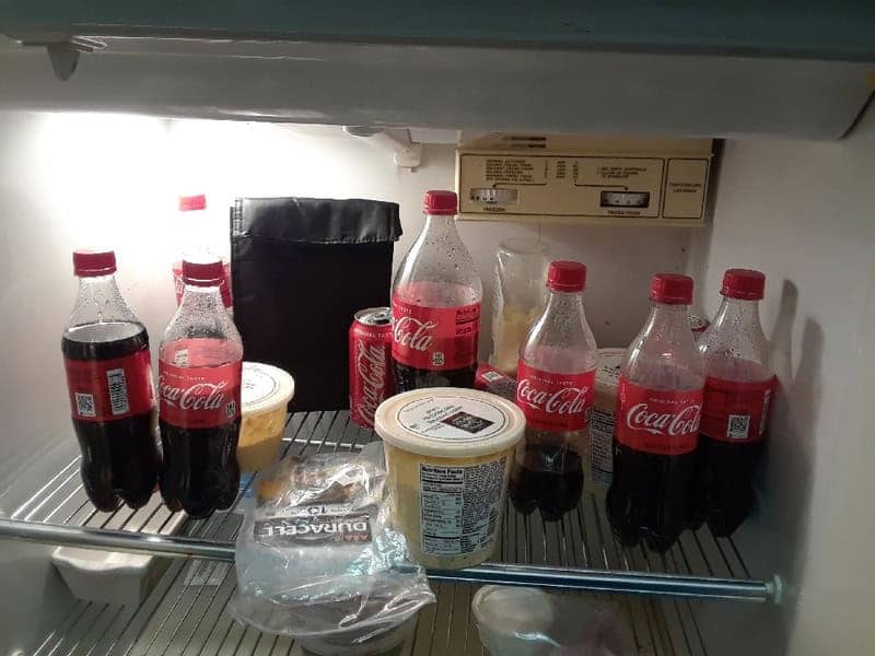 Office fridge hoarded entirely with multiple Coca-Cola bottles and Duracell batteries inside